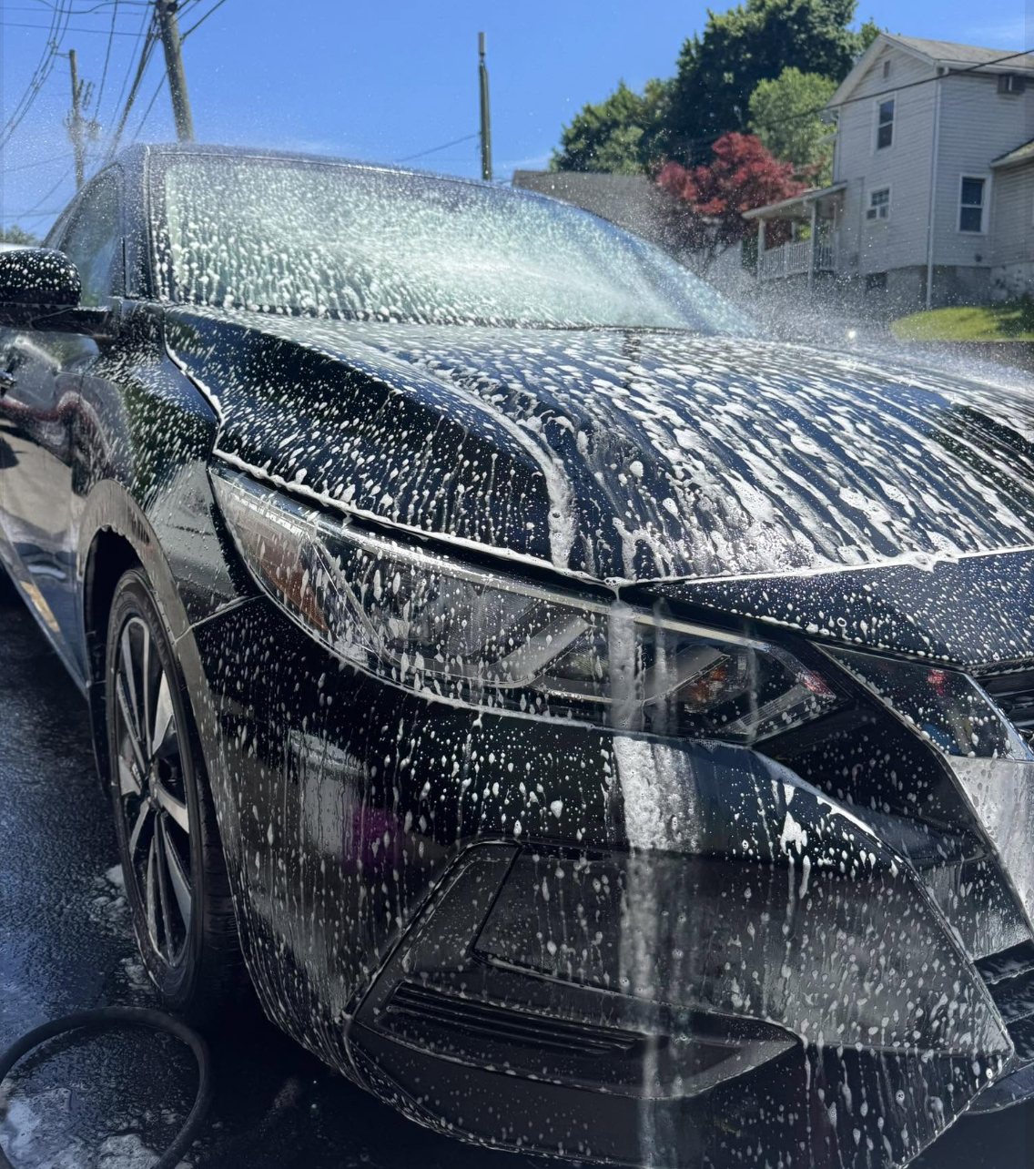Hand wash and foam bath being applied to a dark colored car exterior