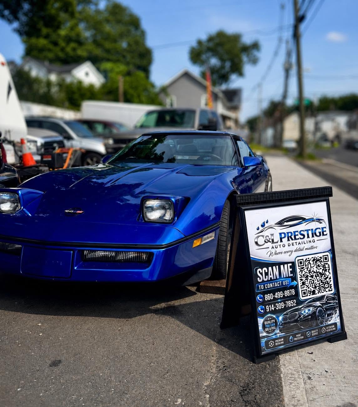 Blue Chevrolet Corvette parked next to the C&L Prestige Auto Detailing sign board