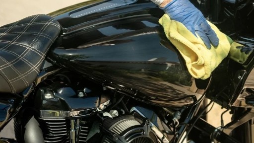 Hand-detailing a glossy black motorcycle gas tank with a yellow microfiber cloth